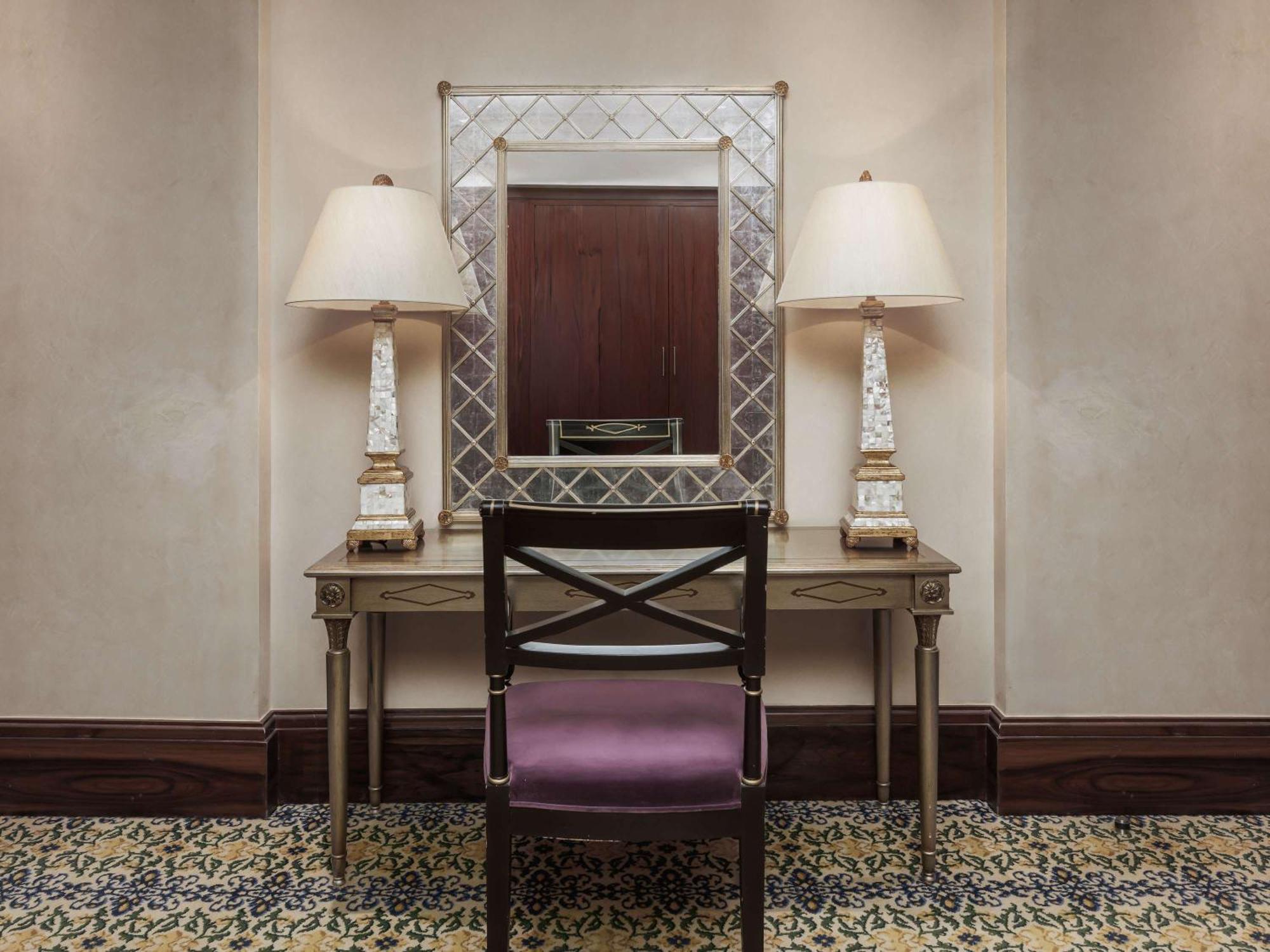 Swissotel Makkah Mecca Exterior photo The photo shows a small, elegantly decorated space featuring a vanity table with a mirror above it. The table is paired with a dark wooden chair that has a purple cushion. On either side of the mirror, there are tall, decorative lamps that provide so