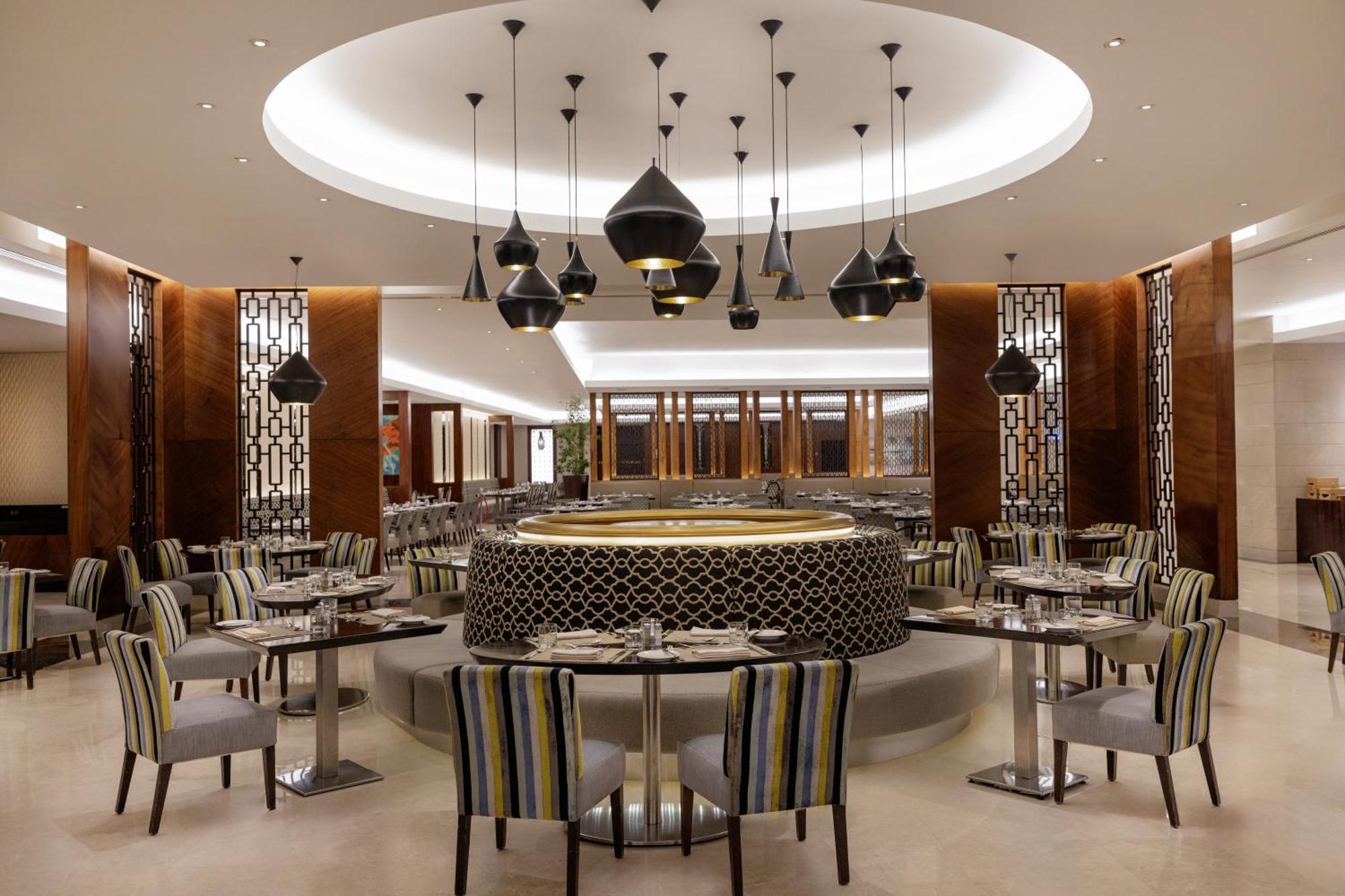 Swissotel Makkah Mecca Exterior photo The photo shows a stylish restaurant interior. It features modern furnishings with circular tables surrounded by striped chairs. The design includes elegant lighting fixtures hanging from a well-lit ceiling, creating a sophisticated atmosphere. The w