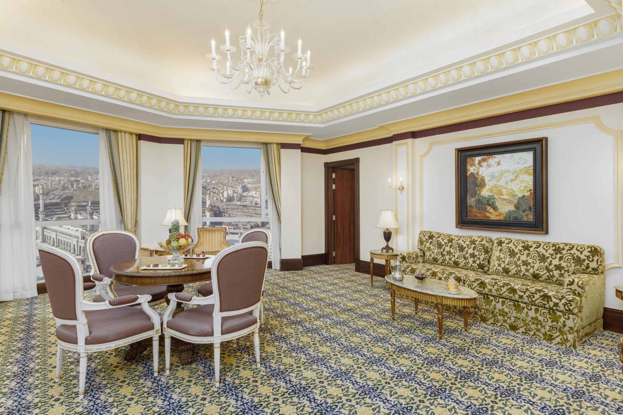 Swissotel Makkah Mecca Exterior photo The photo features an elegantly designed hotel room or suite. It includes:

- A spacious sitting area with a patterned carpet. 
- A green sofa adorned with floral patterns.
- A small table surrounded by four upholstered dining chairs.
- Windows with 