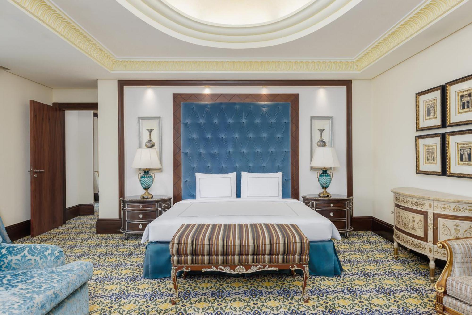Swissotel Makkah Mecca Exterior photo The photo shows an elegantly designed hotel room. Central to the room is a large, comfortable bed with a blue tufted headboard. On either side of the bed are stylish bedside tables with lamps, featuring decorative turquoise bases. A decorative stripe