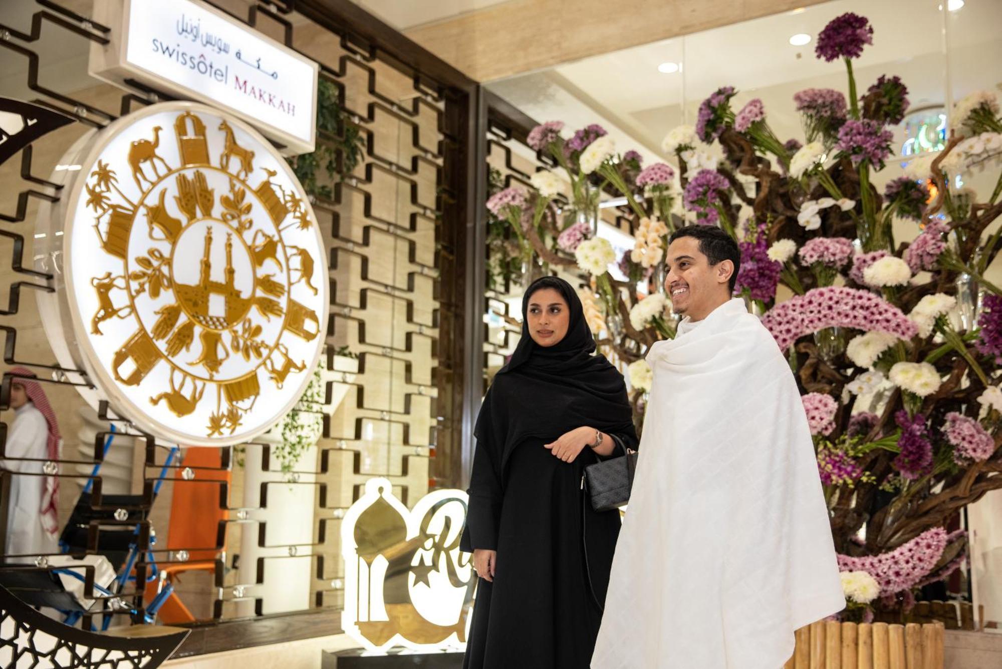 Swissotel Makkah Mecca Exterior photo The photo shows a man and a woman standing together in a decorative setting. The man is wearing a white traditional garment, and the woman is dressed in a black abaya. Behind them, there is an ornate floral arrangement along with a decorative circula